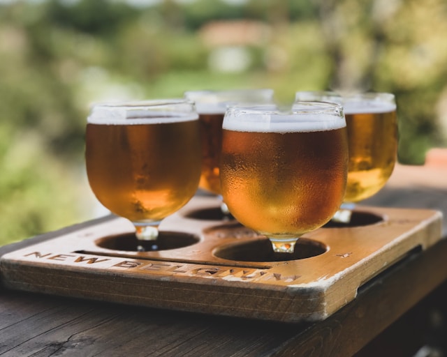 flight of craft beer samples in small glasses on a wooden tasting board outdoors