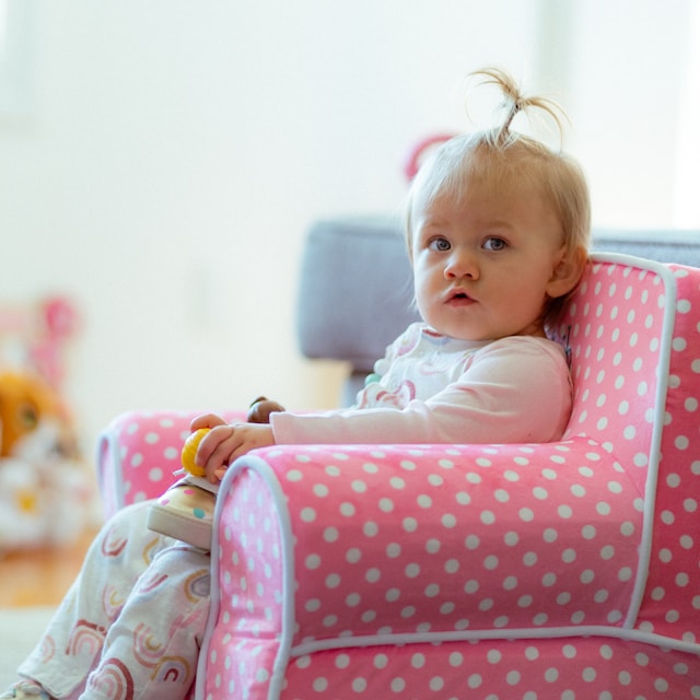 toddler sitting in a pink polka dot armchair holding a toy indoors