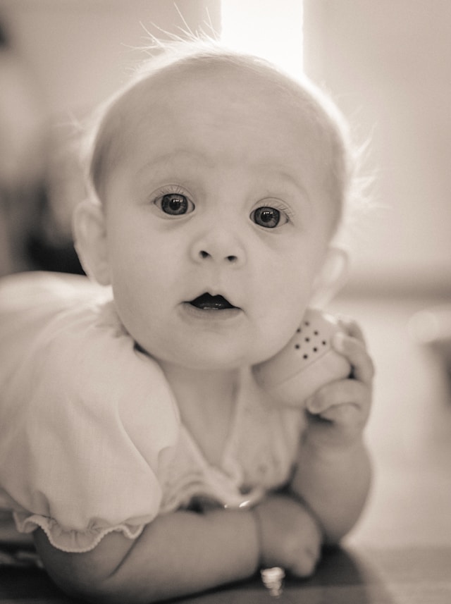 black and white close-up portrait of a baby lying on their stomach and looking at the camera